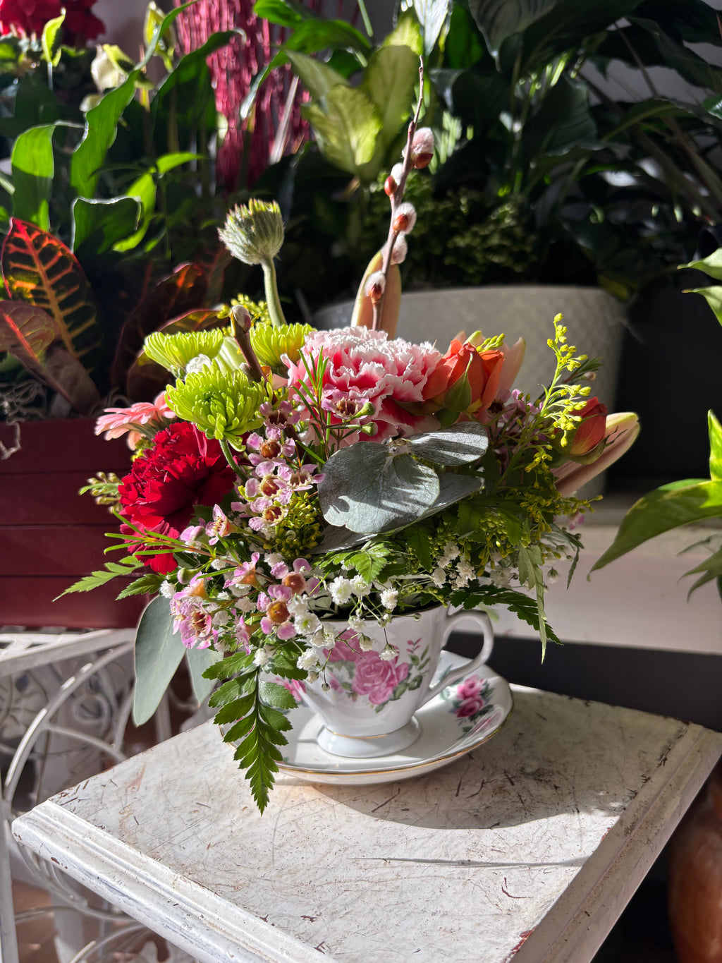 Floral arrangement in a teacup on a table with plants in the background. Mother's Day Flowers Delivered to Mom Hamilton Milton Burlington Oakville Grimsby Toronto