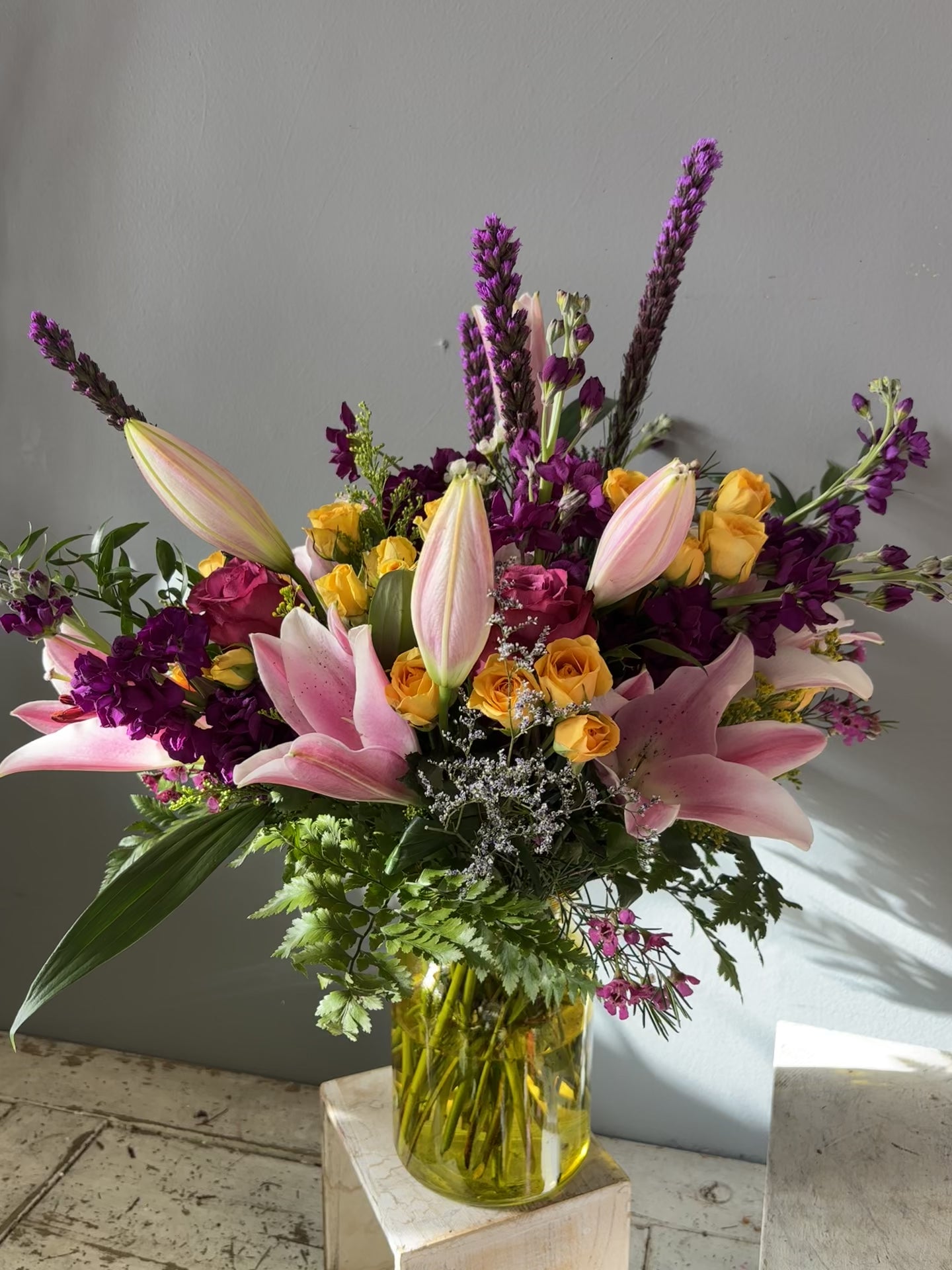 lillies, spray roses, stock, waxflower,  roses in a yellow glass vase