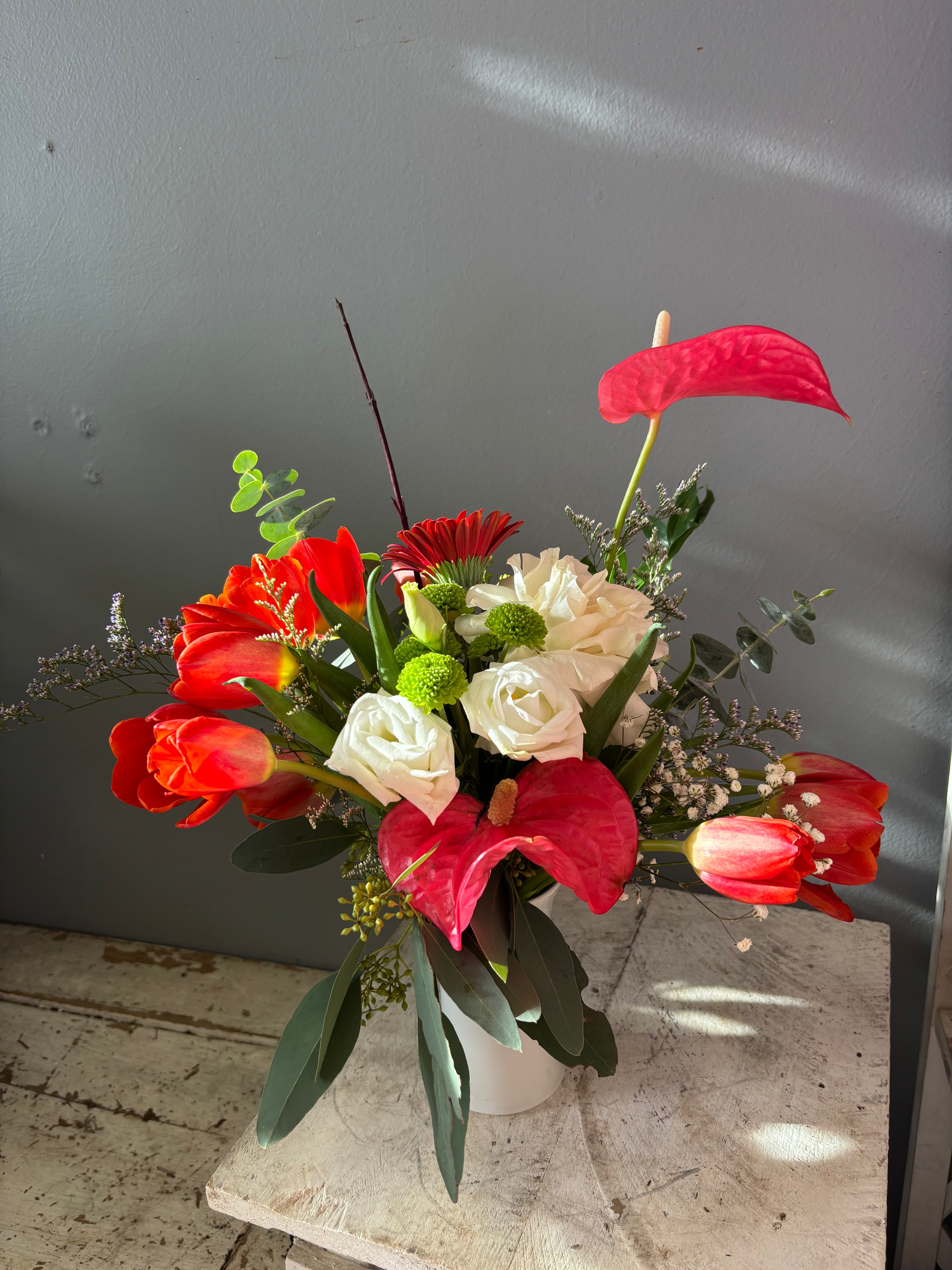 Sculptural anthurium and vivid red tulips reach toward the light alongside a white rose, soft white lisianthus, deep red gerbera, and grounded with seasonal greens.
Designed in a modern white vase, this piece feels expressive and intentional. Simultaneously bold and tender, it’s a reminder not to let the fire burn out, even in seasons of change.

Perfect for moments of encouragement.